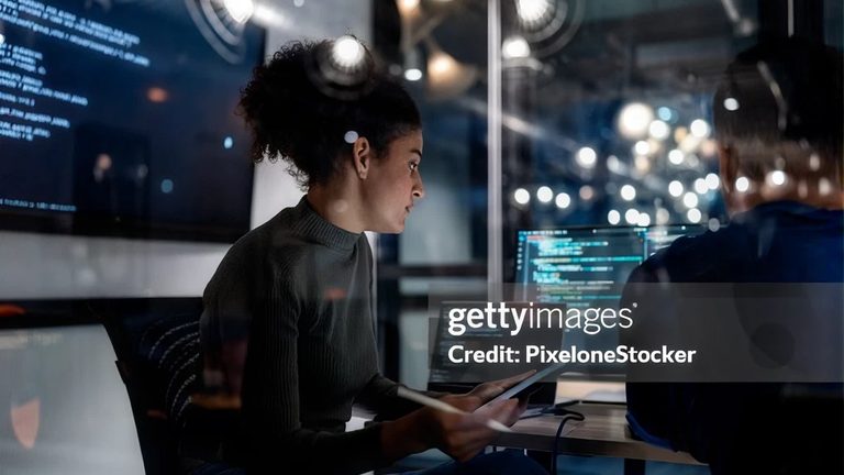 An engineer working at a laptop in front of screens of code