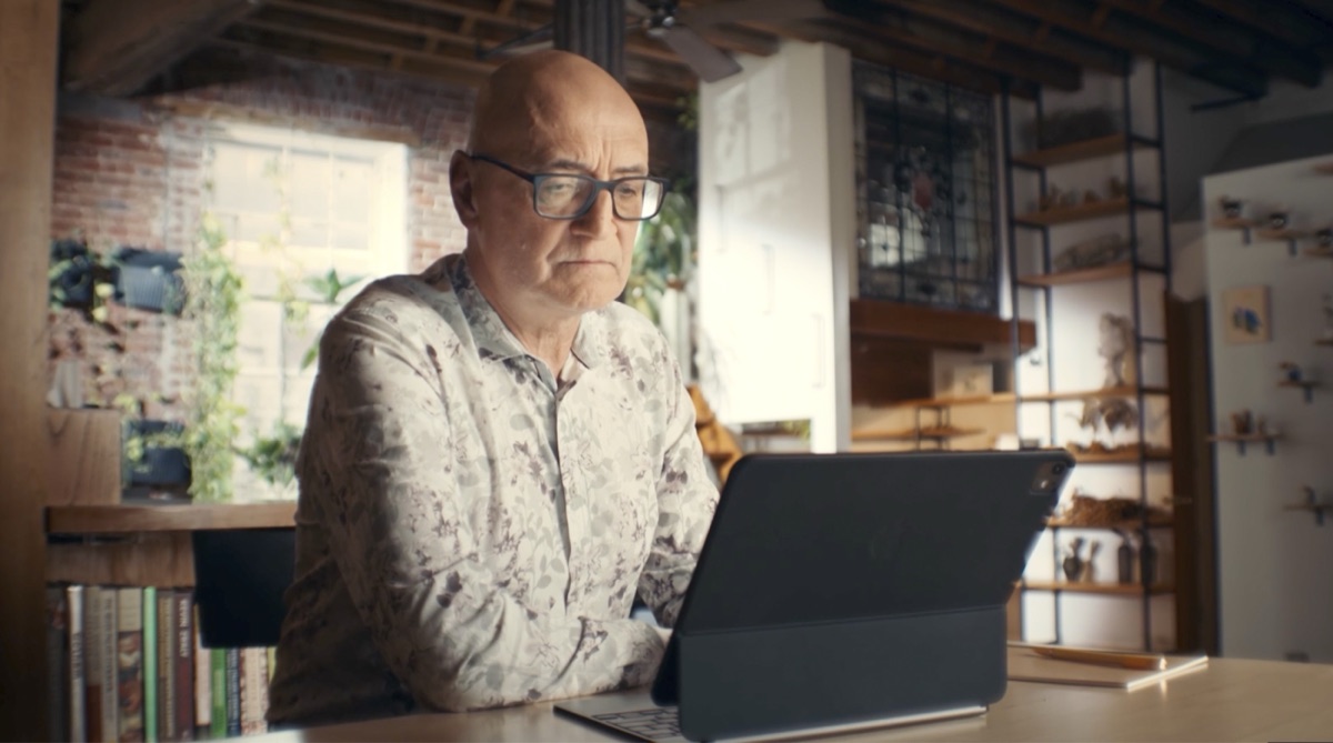 A man in glasses working at a tablet in a sunlit kitchen