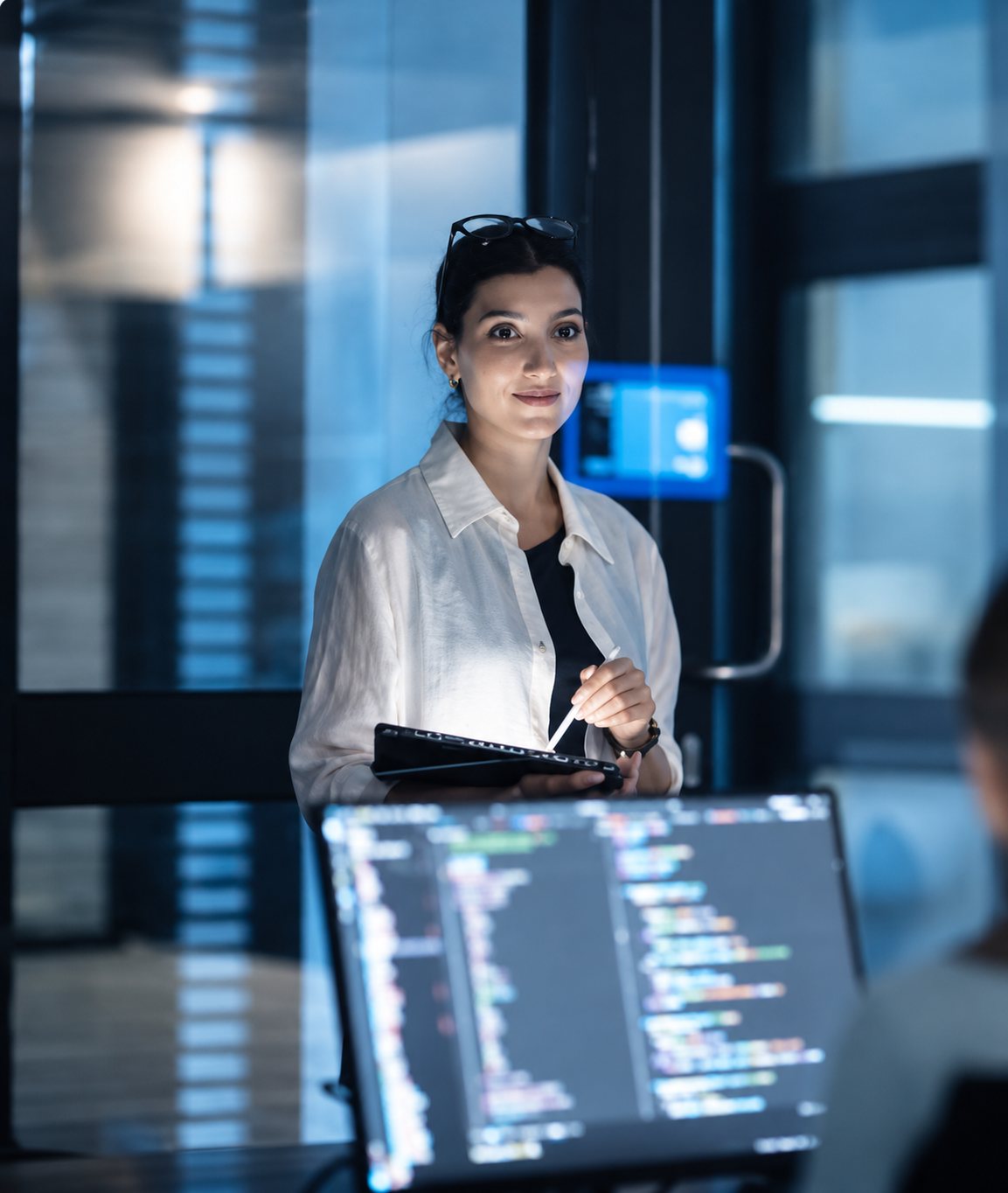 An engineer with a tablet beside screens of code